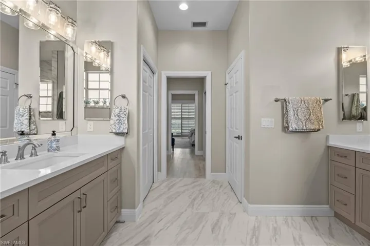 Dual vanity sinks, integrated countertops, framed mirrors, contemporary light fixtures, and marble-finish flooring