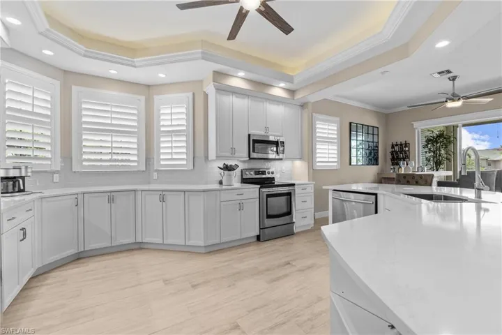 Spacious kitchen featuring light wood-finish flooring, white cabinetry, integrated stainless steel appliances, a large center island with a sink, and crown molding