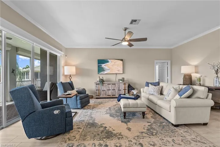 Expansive living area with large format tile flooring, crown molding, and a ceiling fan with integrated lighting