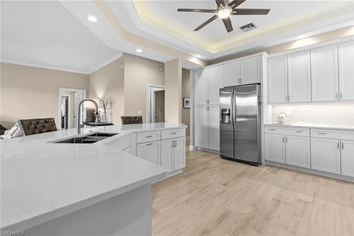White kitchen cabinetry with stainless steel appliances, light-toned wood-finish flooring, a large island with an undermount sink, and recessed ceiling lighting