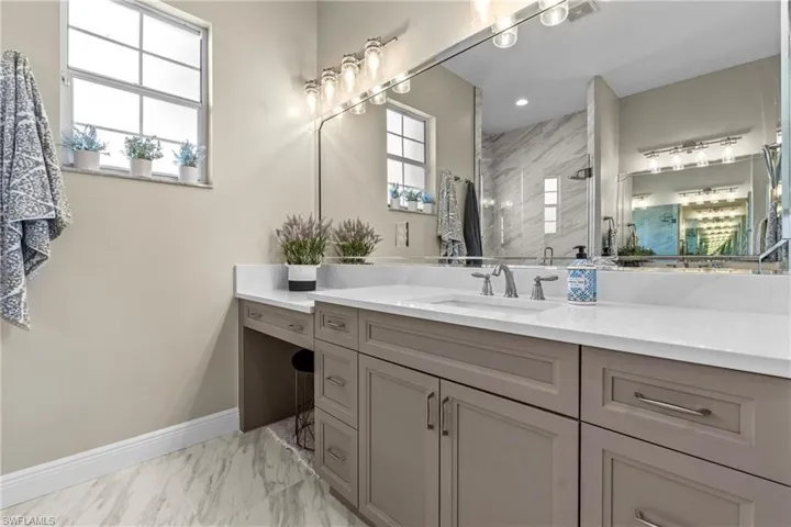 Dual-basin vanity with a makeup counter, white countertops, gray cabinetry, and a large mirror with integrated lighting