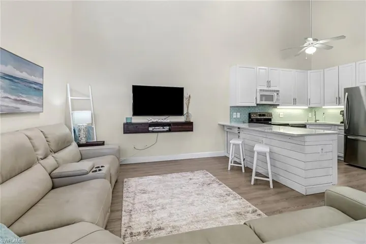 Living area with ceiling fan, a high ceiling, and light wood-style floors