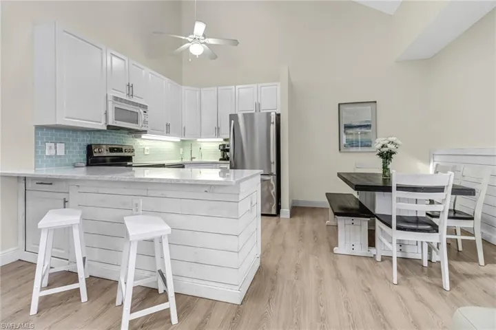 Kitchen with stainless steel appliances, a peninsula, light stone counters, backsplash, and light wood-type flooring