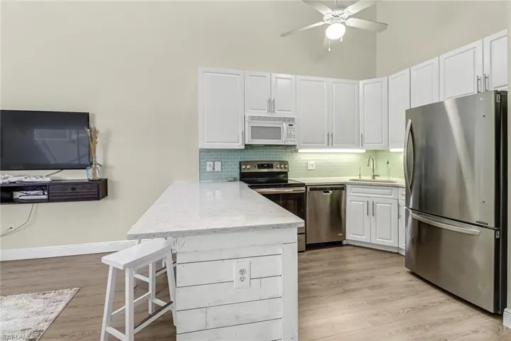 Kitchen with appliances with stainless steel finishes, a breakfast bar, a peninsula, decorative backsplash, and white cabinets