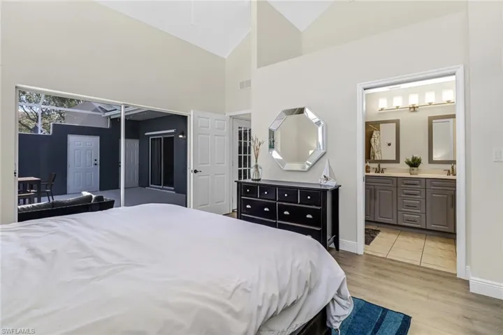 Bedroom with light wood-style floors, high vaulted ceiling, and ensuite bathroom