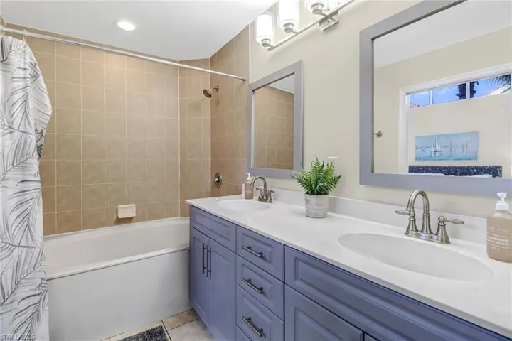Bathroom featuring shower / bath combination with curtain, double vanity, and light tile patterned flooring