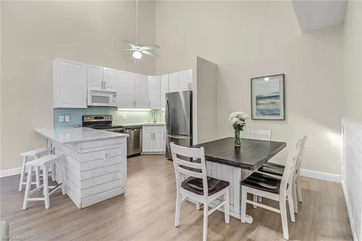Kitchen featuring tasteful backsplash, stainless steel appliances, a kitchen breakfast bar, light wood-style floors, and a high ceiling