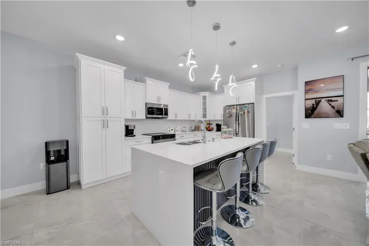 Kitchen featuring a breakfast bar area, white cabinets, stainless steel appliances, light stone counters, and a kitchen island with sink