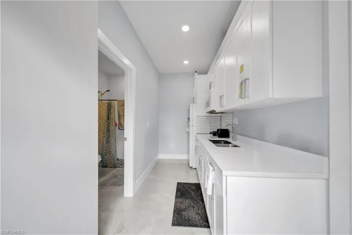 Kitchen featuring light stone countertops, white cabinets, finished concrete floors, tasteful backsplash, and recessed lighting