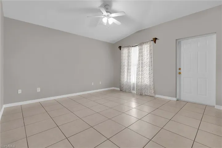 Empty room featuring lofted ceiling, ceiling fan, and light tile patterned floors