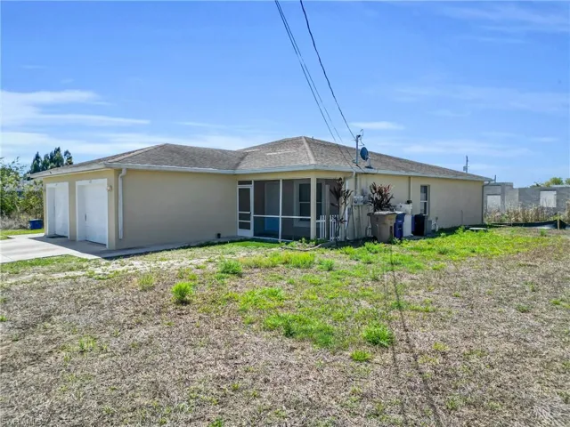 Rear view of house featuring stucco siding, a sunroom, a garage, and driveway