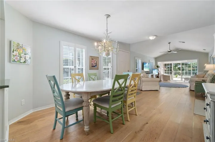 Dining space featuring ceiling fan with notable chandelier, light hardwood / wood-style floors, and lofted ceiling
