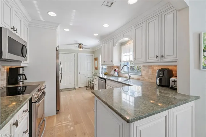 Kitchen with white cabinetry, sink, ceiling fan, stainless steel appliances, and backsplash