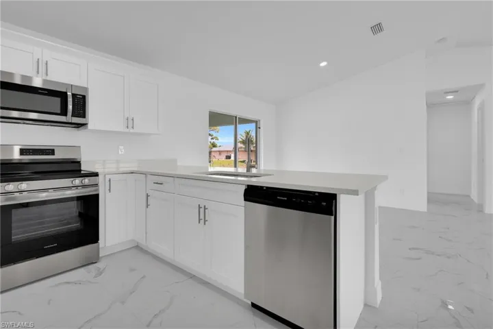 Kitchen featuring white shaker cabinetry, stainless steel appliances, light-toned countertops, and white tile flooring