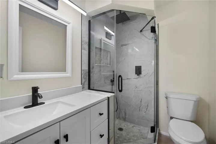Bathroom featuring a shower with shower door, toilet, and vanity