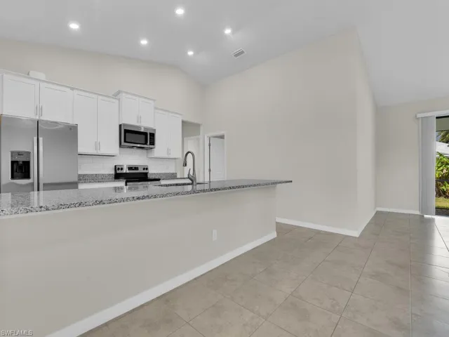 Kitchen featuring light stone countertops, appliances with stainless steel finishes, sink, lofted ceiling, and white cabinets