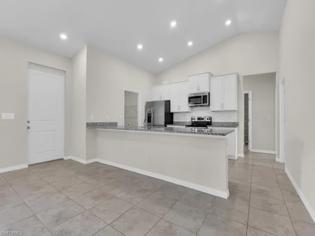Kitchen featuring white cabinetry, light tile patterned floors, kitchen peninsula, light stone countertops, and appliances with stainless steel finishes