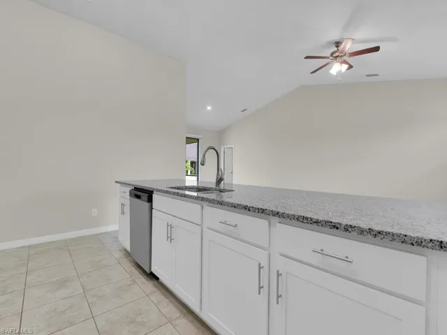 Kitchen with light stone counters, sink, ceiling fan, vaulted ceiling, and white cabinets