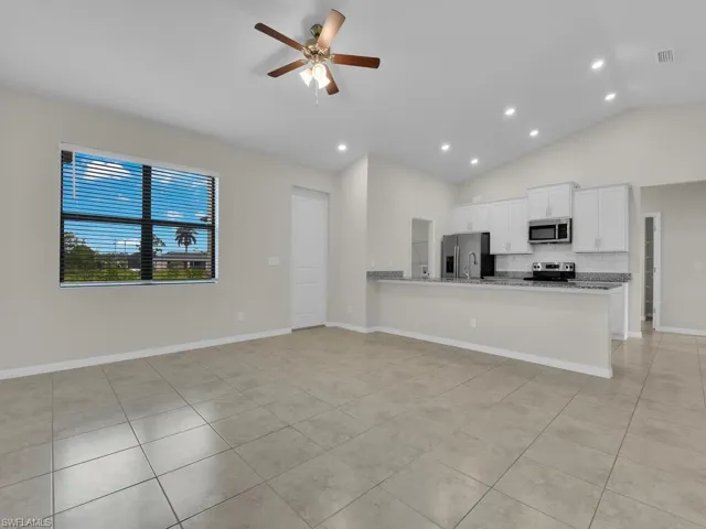 Kitchen with stainless steel appliances, kitchen peninsula, white cabinetry, ceiling fan, and light stone counters