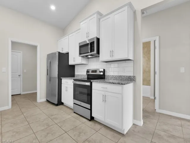 Kitchen with vaulted ceiling, light stone countertops, appliances with stainless steel finishes, and white cabinets