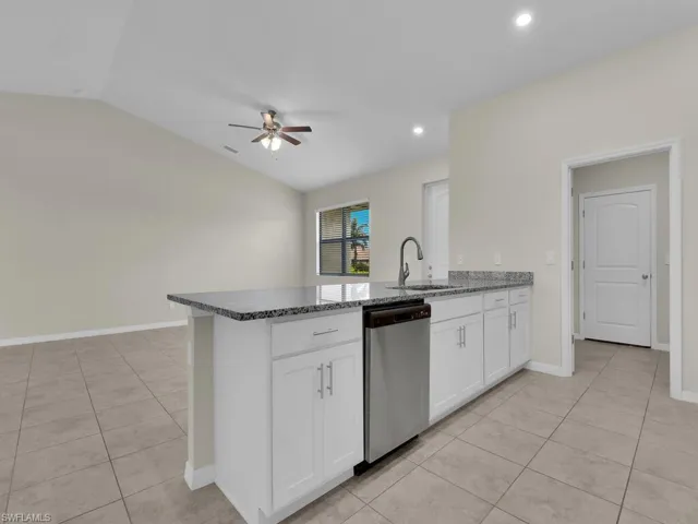 Kitchen featuring vaulted ceiling, white cabinetry, sink, ceiling fan, and stainless steel dishwasher