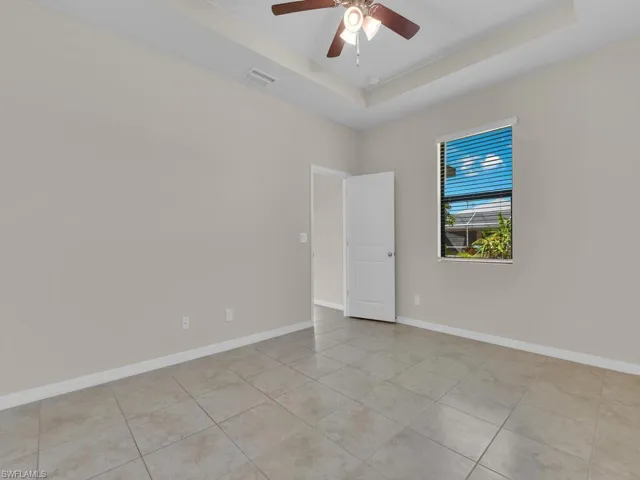 Empty room featuring a tray ceiling, light tile patterned floors, and ceiling fan