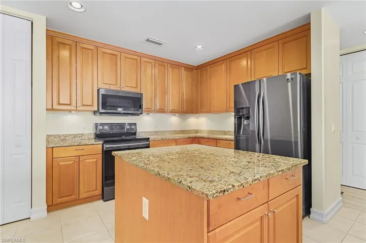 Kitchen featuring light tile patterned floors, appliances with stainless steel finishes, light stone counters, and visible vents
