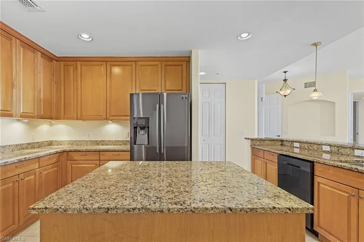 Kitchen with a kitchen island, stainless steel refrigerator with ice dispenser, and light stone counters