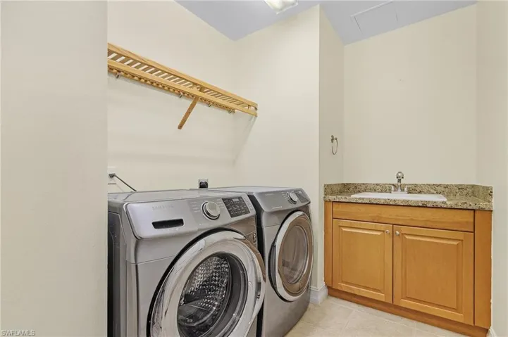 Clothes washing area featuring washing machine and clothes dryer, cabinet space, a sink, and light tile patterned floors