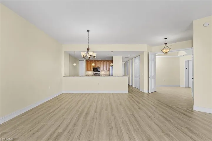 Unfurnished living room with light wood-style flooring, a notable chandelier, and baseboards