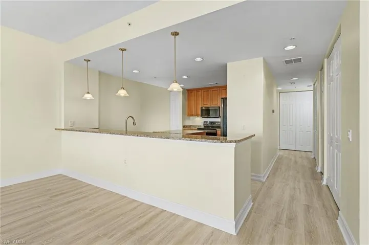 Kitchen with stone countertops, brown cabinetry, light wood-style flooring, stainless steel appliances, and visible vents