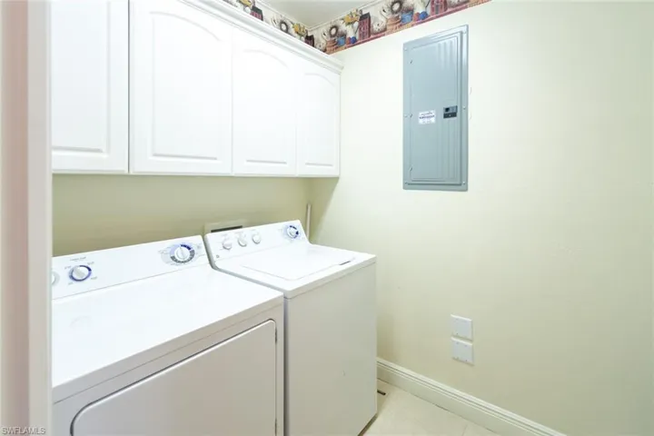 Washroom featuring electric panel, washer and dryer, light tile patterned flooring, and cabinet space