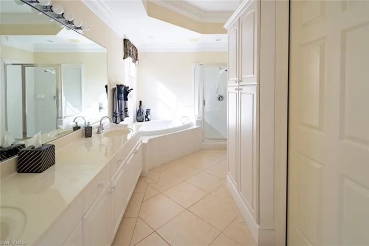Full bathroom featuring light tile patterned flooring, a shower stall, double vanity, a bath, and crown molding