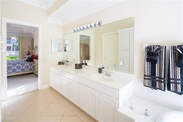 Bathroom featuring double vanity, ensuite bathroom, light tile patterned floors, ornamental molding, and a bath