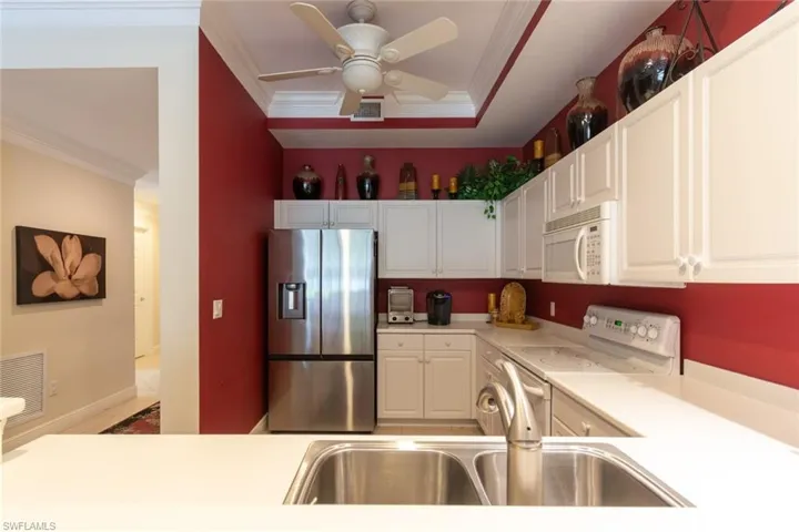 Kitchen featuring white appliances, crown molding, light countertops, white cabinetry, and a ceiling fan