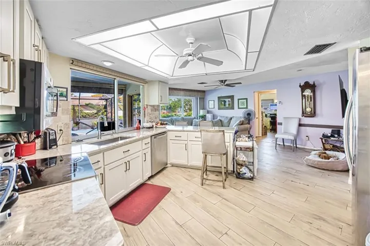 Kitchen with open floor plan, white cabinets, stainless steel appliances, a peninsula, and light stone counters