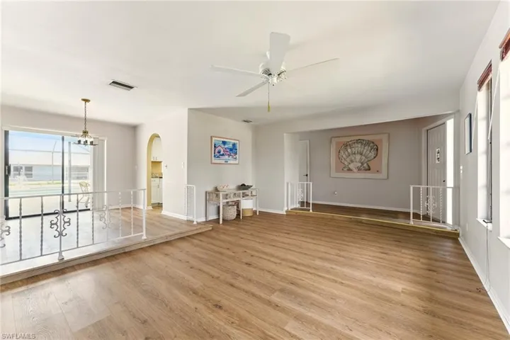 Unfurnished living room with ceiling fan, light luxury vinyl  floors, and arched walkway into the kitchen - sliders to the outside lanai