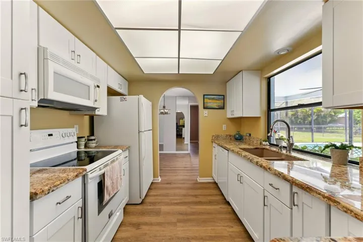 Kitchen featuring white appliances, arched walkways, white cabinetry, granite countertops, and lvp flooring