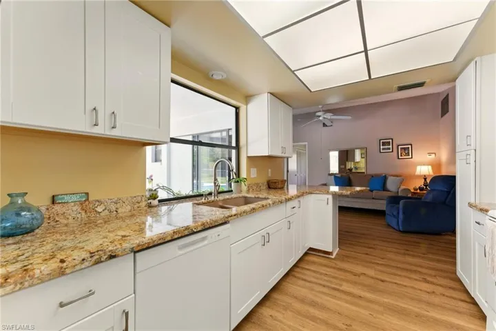 Kitchen with white dishwasher, open floor plan, white cabinets, lvp flooring, granite   countertops