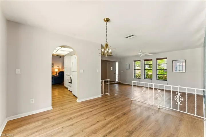 Unfurnished living room with lvp flooring, arched walkways, ceiling fan, and a chandelier