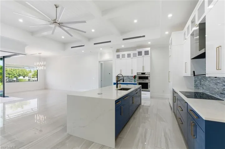 Kitchen with white cabinets, beam ceiling, glass insert cabinets, backsplash, and a chandelier