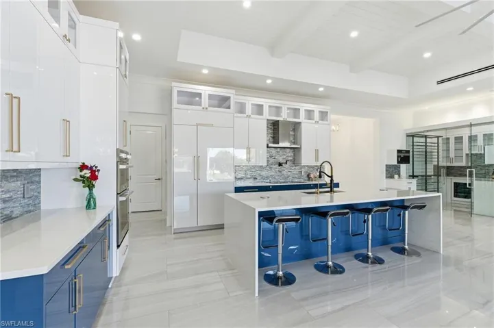 Kitchen with glass insert cabinets, white cabinetry, recessed lighting, a center island with sink, and decorative backsplash