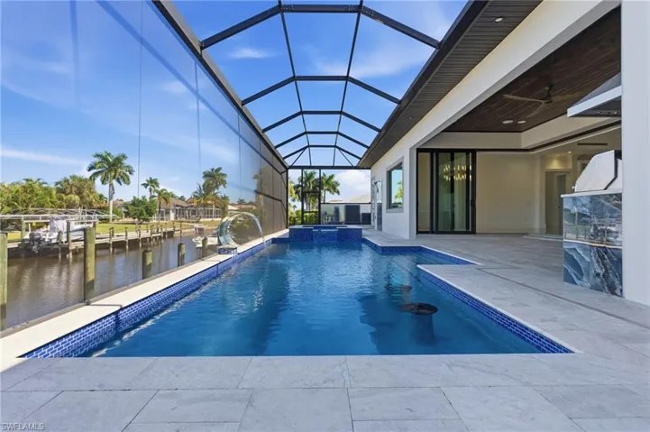 View of swimming pool featuring a sunroom, a patio area, a pool with connected hot tub, glass enclosure, and a water view