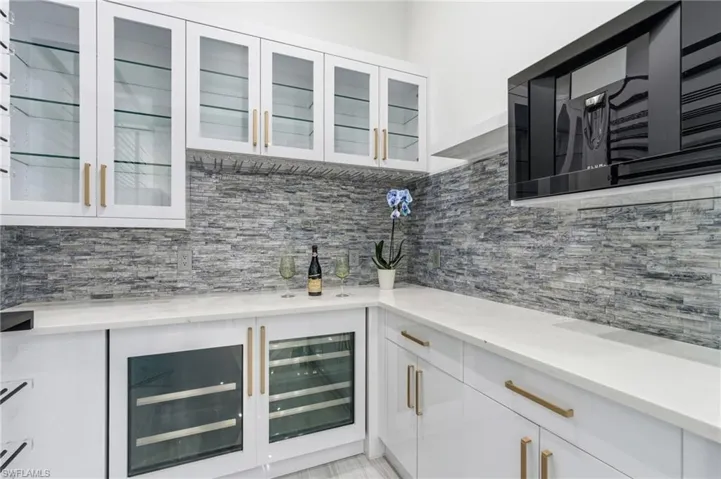 Bar featuring white cabinetry, black microwave, light stone countertops, and beverage cooler