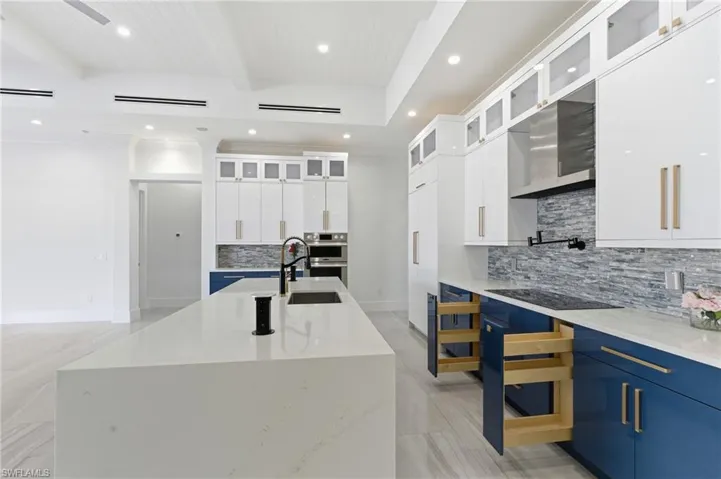 Kitchen with white cabinets, beam ceiling, light stone counters, decorative backsplash, and recessed lighting