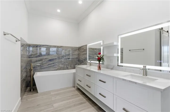 Full bathroom featuring double vanity, a freestanding tub, ornamental molding, and light wood-type flooring