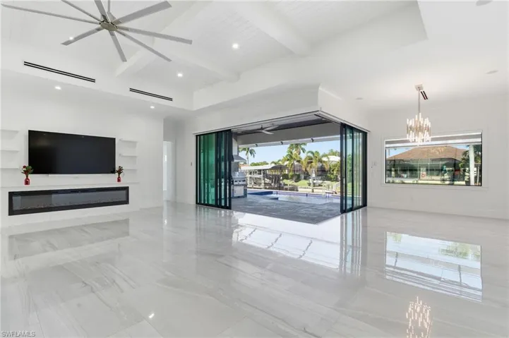 Unfurnished living room with beam ceiling, coffered ceiling, a glass covered fireplace, a chandelier, and a ceiling fan