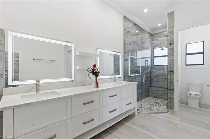 Full bathroom featuring double vanity, a marble finish shower, and recessed lighting