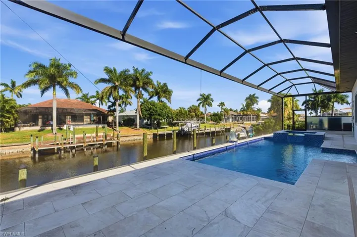 View of swimming pool with a sunroom, a pool with connected hot tub, glass enclosure, a water view, and a patio