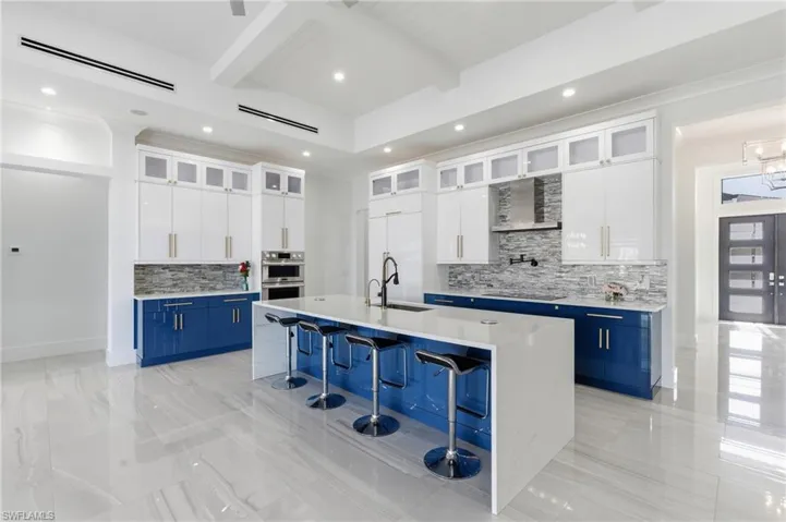 Kitchen with beamed ceiling, white cabinetry, blue cabinetry, glass insert cabinets, and recessed lighting